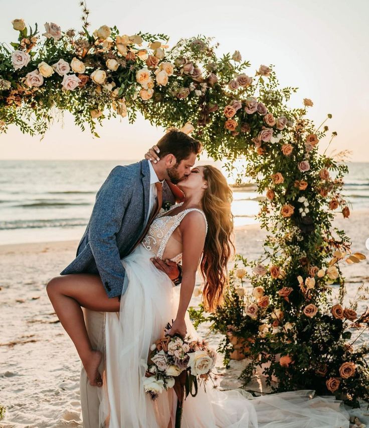 symbolic ceremony A couple shares a tender kiss under a wedding arch at sunset by the sea, capturing a deeply emotional and symbolic moment.
