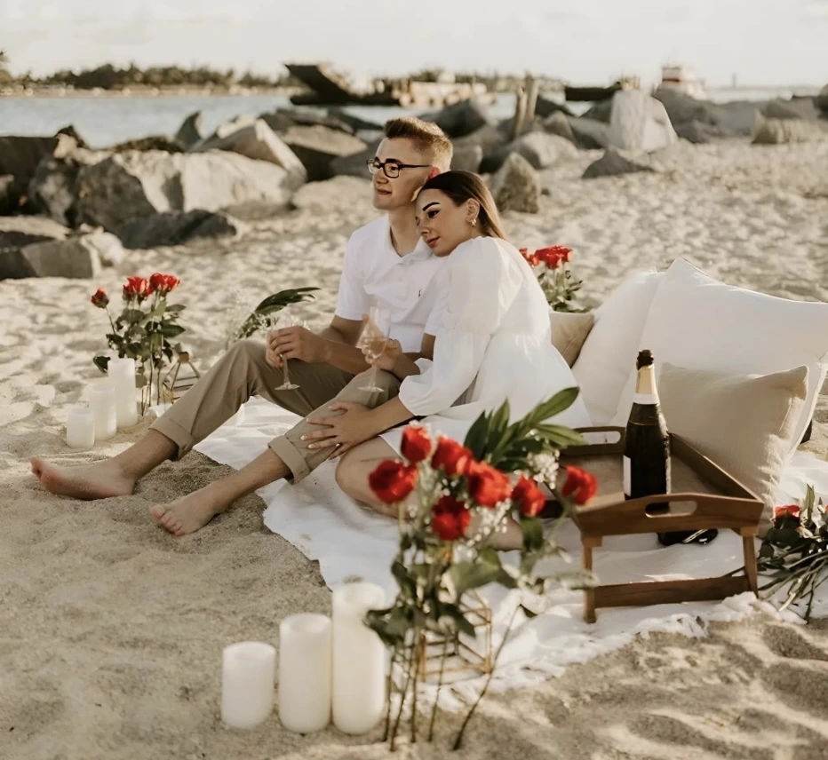 Romantic proposal setup on a Crete beach — couple sitting together surrounded by candles, rose petals and cushions by the sea, organized by WedSpace proposal planner in Rethymno.