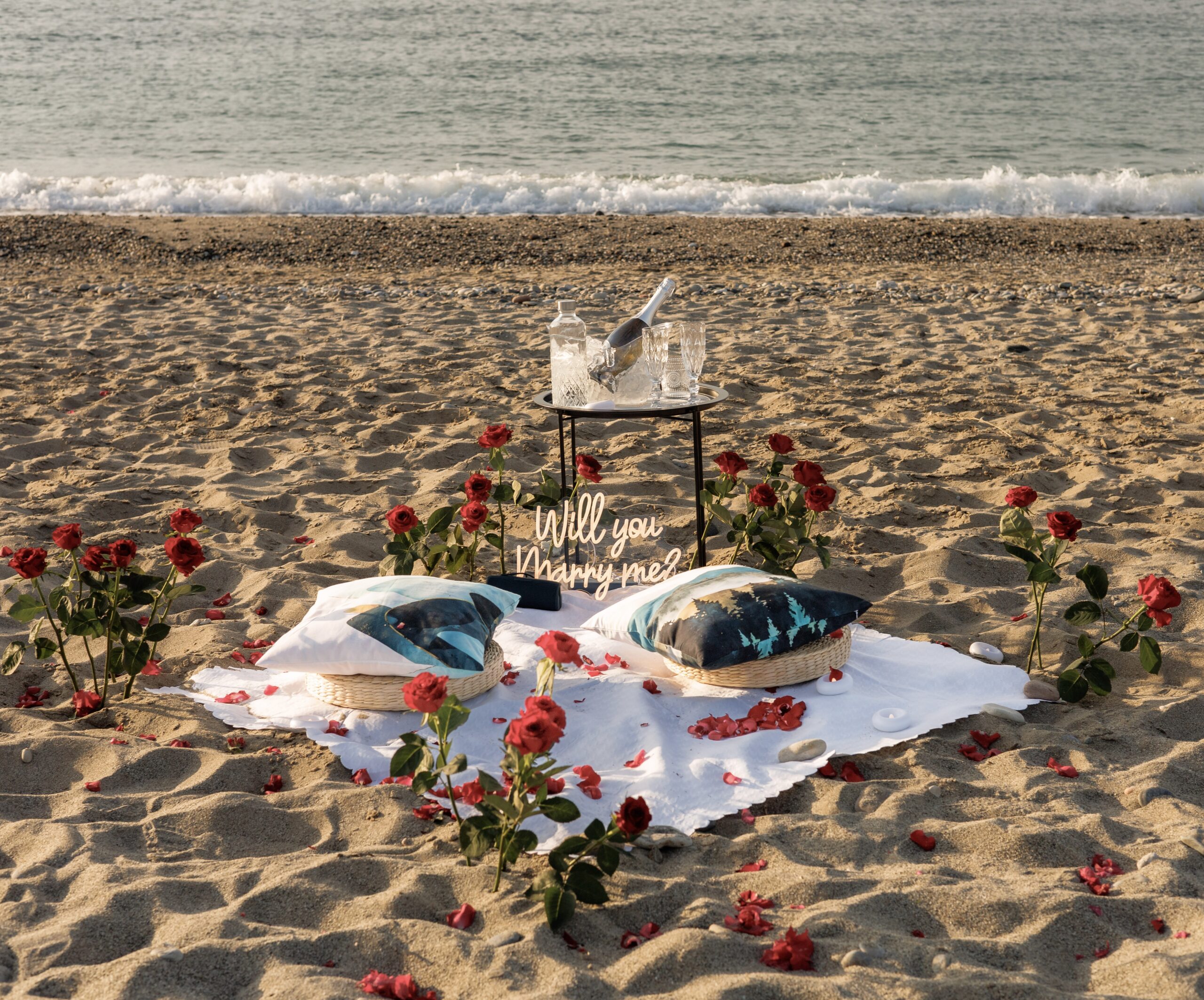 Minimalist beach proposal setup in Crete featuring romantic lanterns, floor cushions, and sunset champagne for Essential package from Wedspace Crete