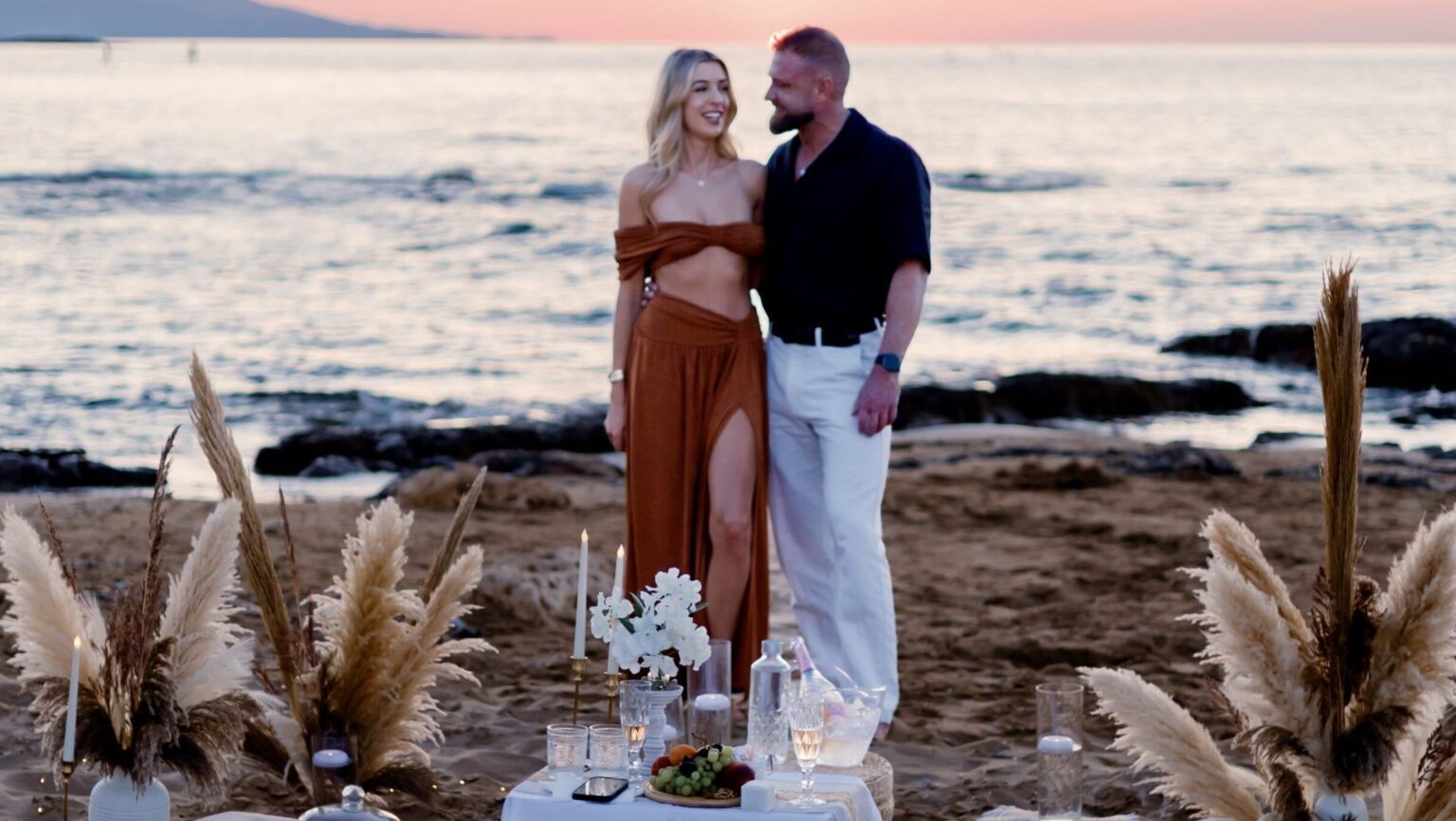 Surprise beach proposal in Crete featuring a romantic setup with pampas grass, boho decor, and sunset sea view by WedSpace Crete