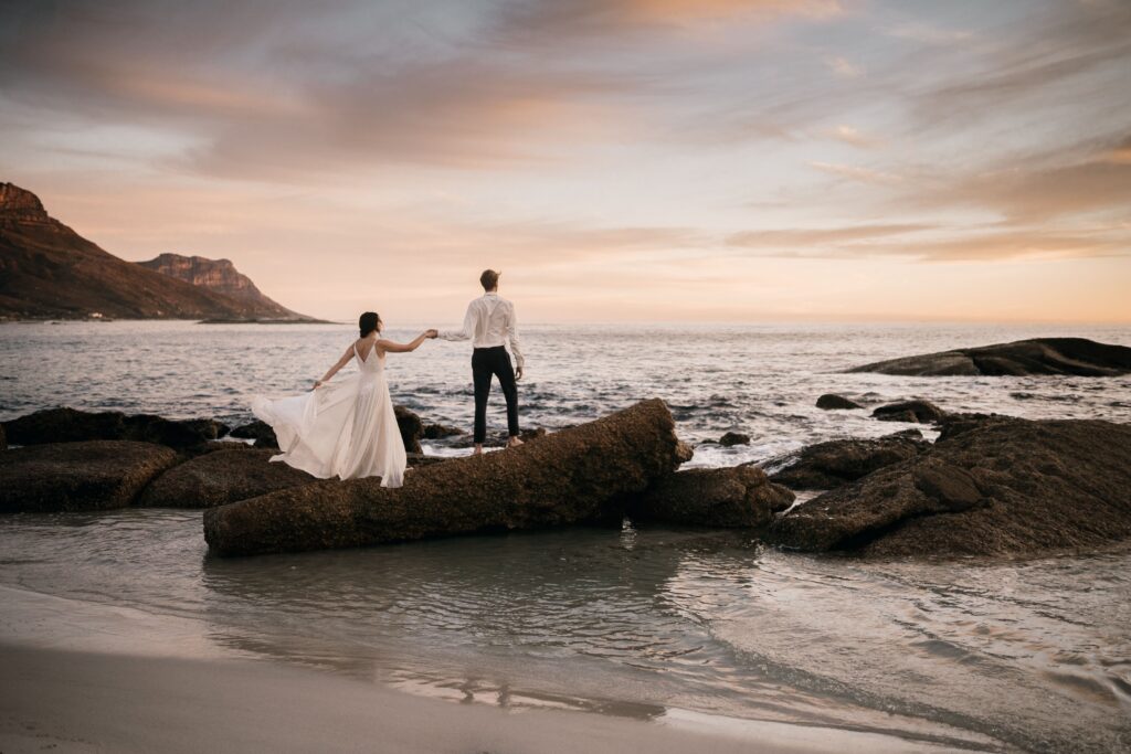 Romantic couple holding hands on coastal rocks during a sunset beach elopement in Crete, organized by Wed-Space.