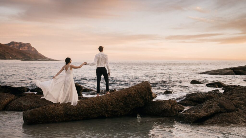 Romantic couple holding hands on coastal rocks during a sunset beach elopement in Crete, organized by Wed-Space.