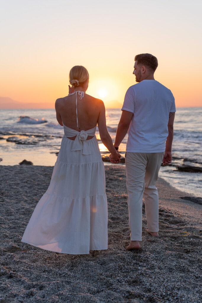 Romina and Keno walking hand-in-hand along the shoreline after beach proposal in Rethymno, Crete⁠