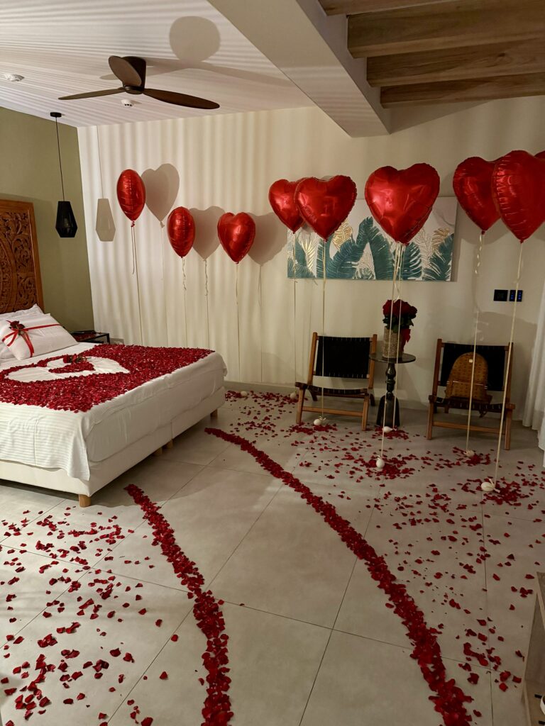Romantic surprise hotel room decoration in Crete with rose petals on the bed and red heart balloons, arranged by WedSpace.