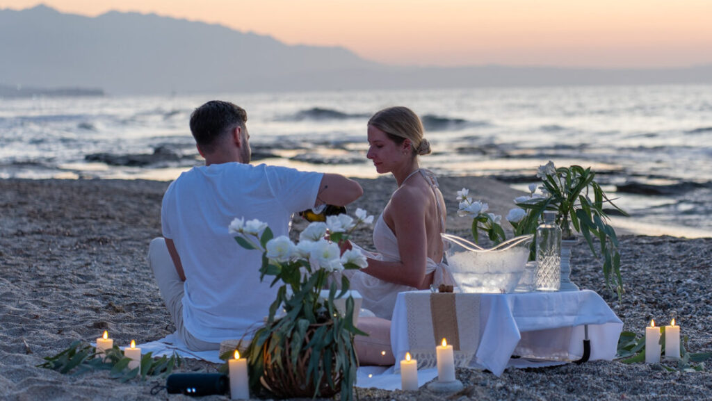 Boho-style beach proposal setup with champagne, candles, and flowers in Rethymno by WedSpace Crete⁠