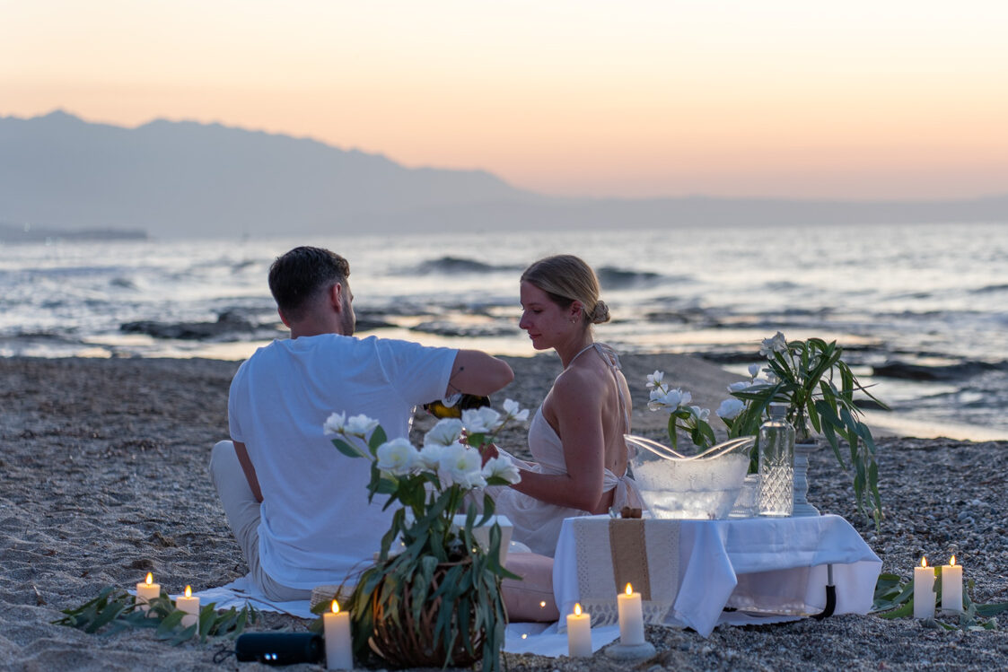 Boho-style beach proposal setup with champagne, candles, and flowers in Rethymno by WedSpace Crete⁠