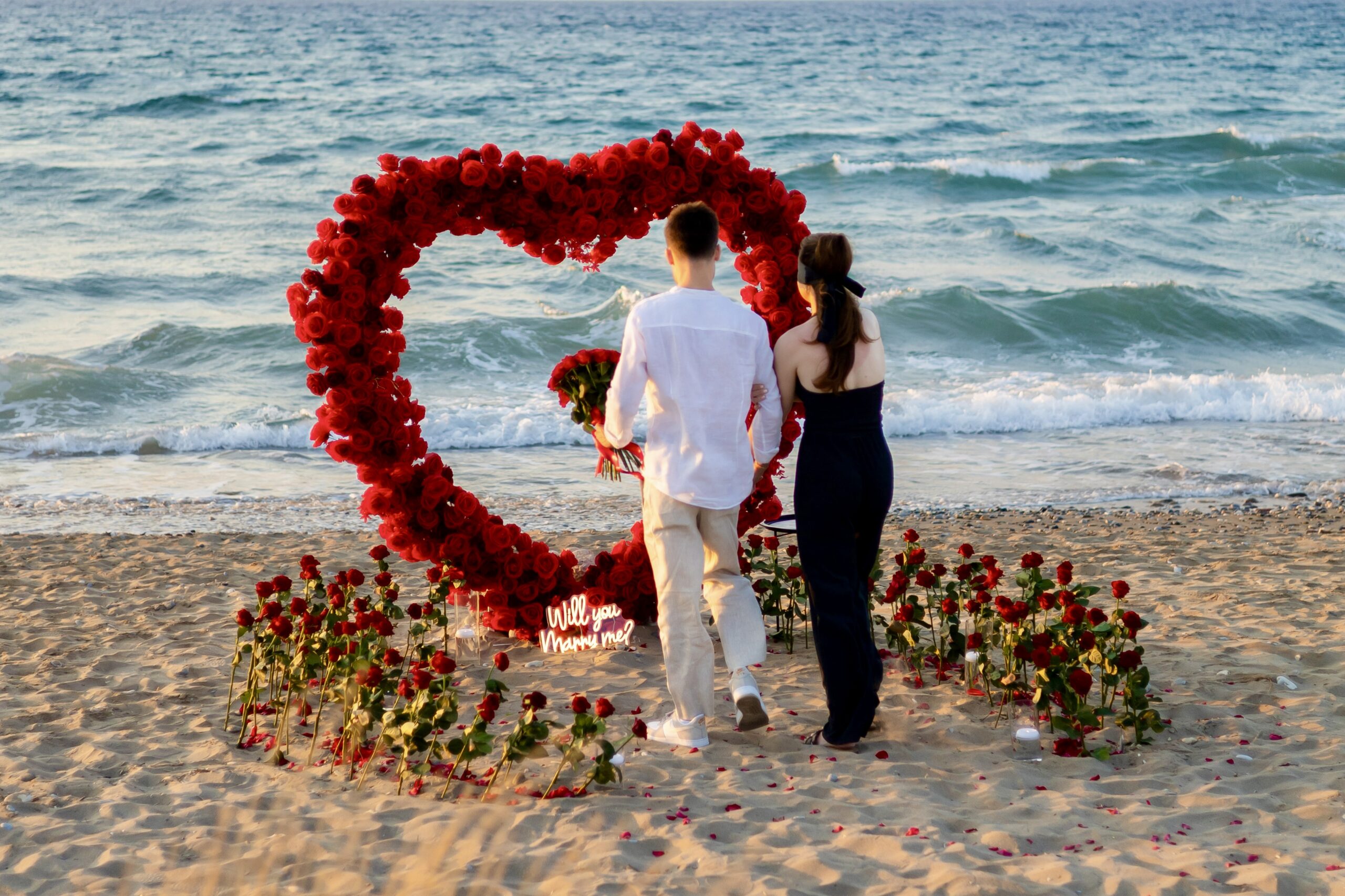 Couple walking on Georgioupoli beach, Crete, during golden hour with a romantic proposal setup in the background by WedSpace.